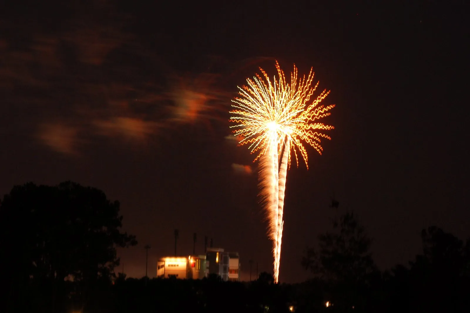 A firework bursts over a lighted stadium press box on the night of July 4, 2010.