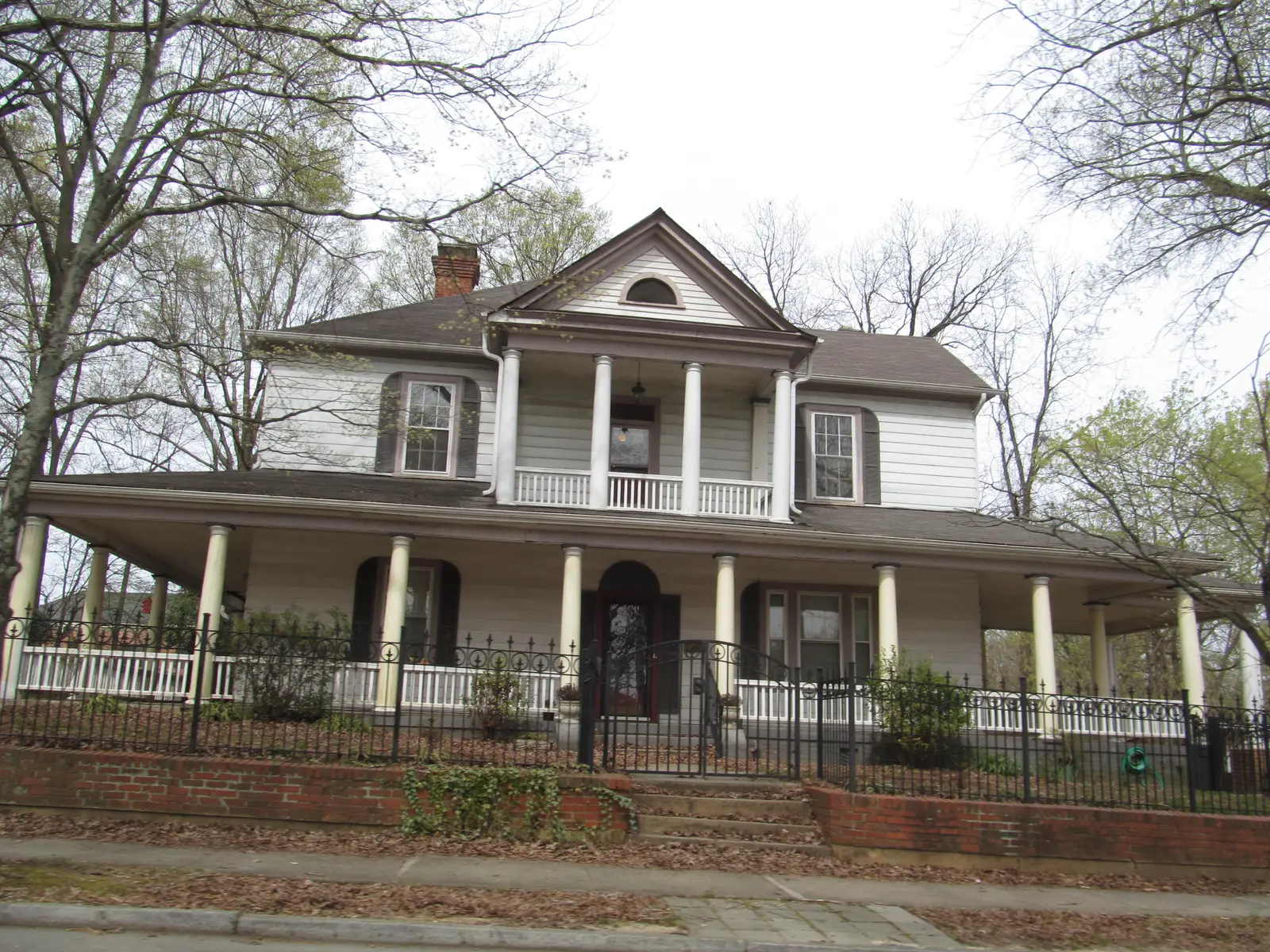 A two-story frame house with a wraparound porch and an iron fence among the older homes of Wake Forest's historic core.